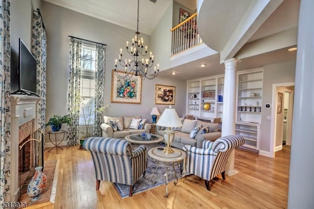 living room with decorative columns, a brick fireplace, a notable chandelier, wood-type flooring, and high vaulted ceiling