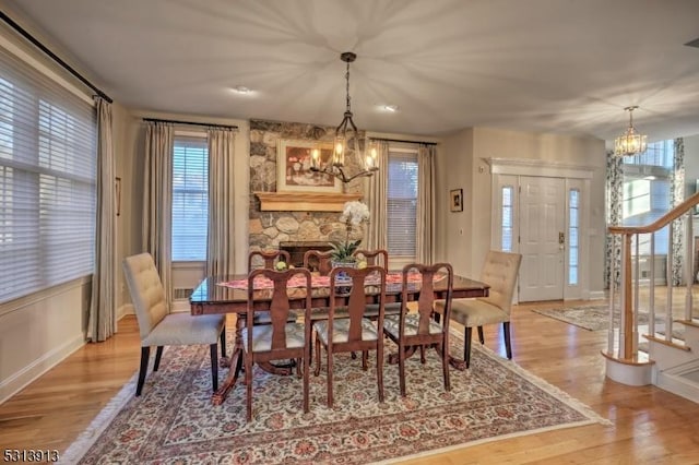 dining room with light hardwood / wood-style flooring, a stone fireplace, and an inviting chandelier