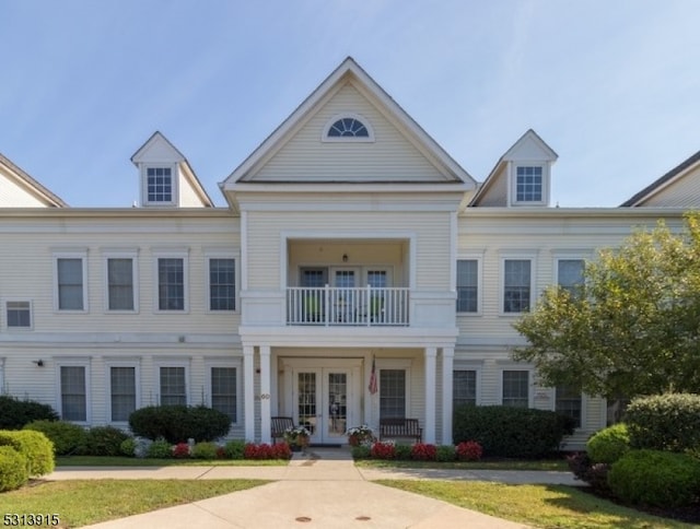 view of front of house with a balcony, french doors, and a front lawn