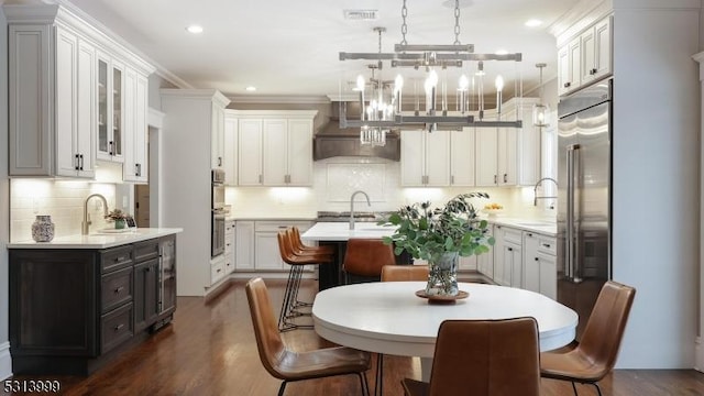 kitchen with wall chimney exhaust hood, white cabinetry, and decorative light fixtures