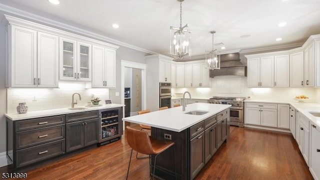 kitchen with appliances with stainless steel finishes, wine cooler, sink, a kitchen island with sink, and custom range hood