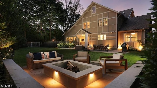 back house at dusk with a lawn, a patio, and an outdoor living space with a fire pit