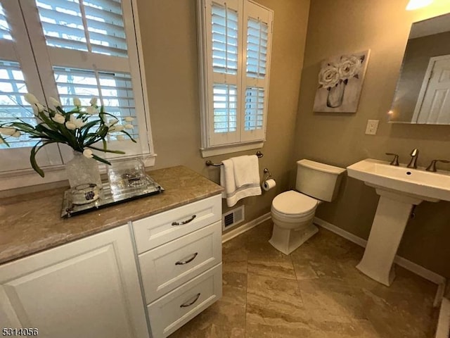 half bath with toilet, a sink, visible vents, and baseboards