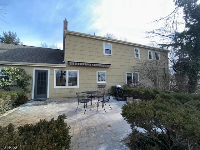 back of property featuring roof with shingles, a chimney, and a patio area