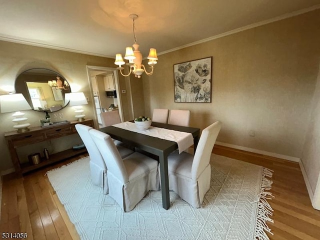 dining room with baseboards, ornamental molding, light wood-style flooring, and an inviting chandelier