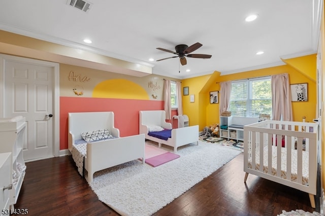 bedroom with a crib, ornamental molding, dark hardwood / wood-style flooring, and ceiling fan