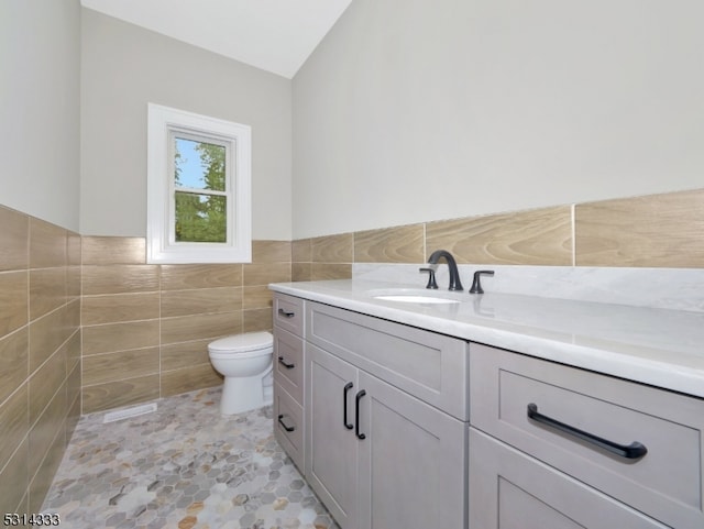 bathroom featuring tile walls, vanity, lofted ceiling, tile patterned flooring, and toilet