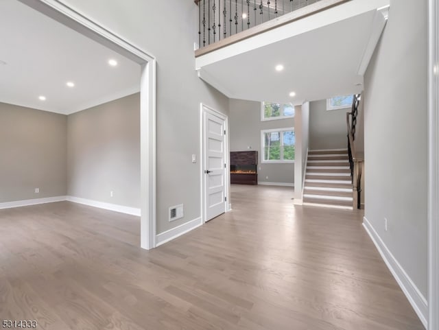 entrance foyer featuring light hardwood / wood-style flooring, a towering ceiling, and ornamental molding