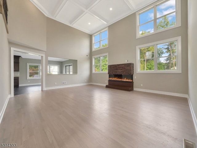 unfurnished living room featuring light hardwood / wood-style flooring, a high ceiling, coffered ceiling, and a stone fireplace