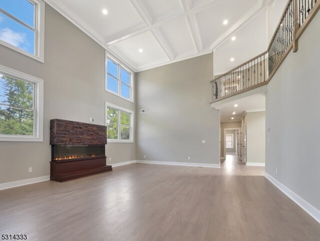 unfurnished living room with a fireplace, beamed ceiling, wood-type flooring, a high ceiling, and crown molding