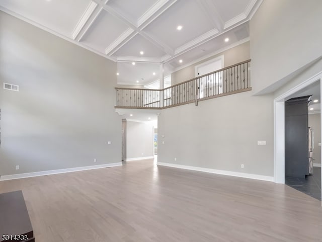 unfurnished living room featuring wood-type flooring, beamed ceiling, a towering ceiling, and coffered ceiling