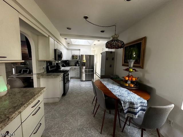 kitchen featuring appliances with stainless steel finishes, white cabinets, tasteful backsplash, stone counters, and a skylight