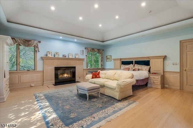 bedroom featuring a tray ceiling, light hardwood / wood-style floors, and multiple windows