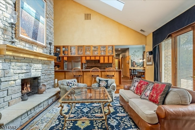 living room featuring hardwood / wood-style flooring, a stone fireplace, a skylight, and high vaulted ceiling