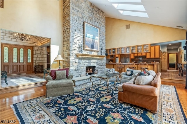 living room featuring high vaulted ceiling, wood-type flooring, a skylight, and a fireplace