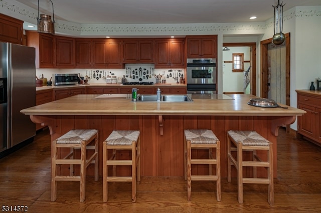 kitchen featuring sink, appliances with stainless steel finishes, an island with sink, and dark hardwood / wood-style flooring