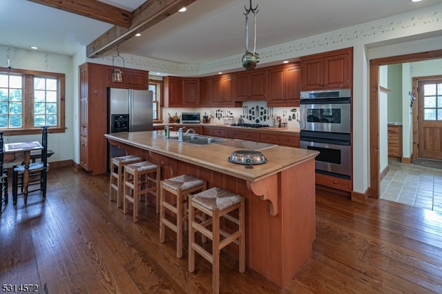 kitchen with a kitchen island with sink, stainless steel appliances, dark wood-type flooring, sink, and decorative light fixtures