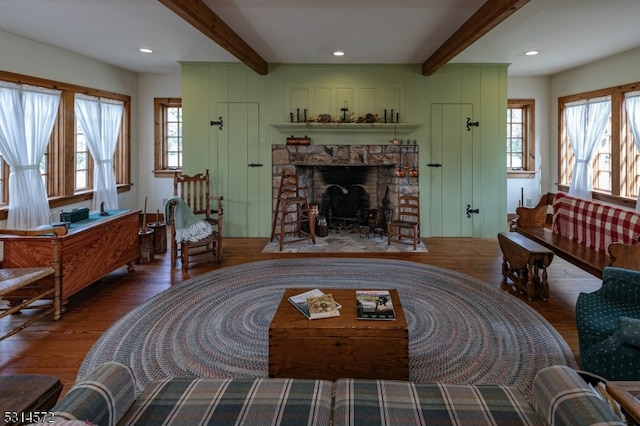 living room featuring a healthy amount of sunlight, beamed ceiling, wood-type flooring, and a stone fireplace