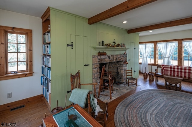 living room with beamed ceiling, a stone fireplace, and wood-type flooring