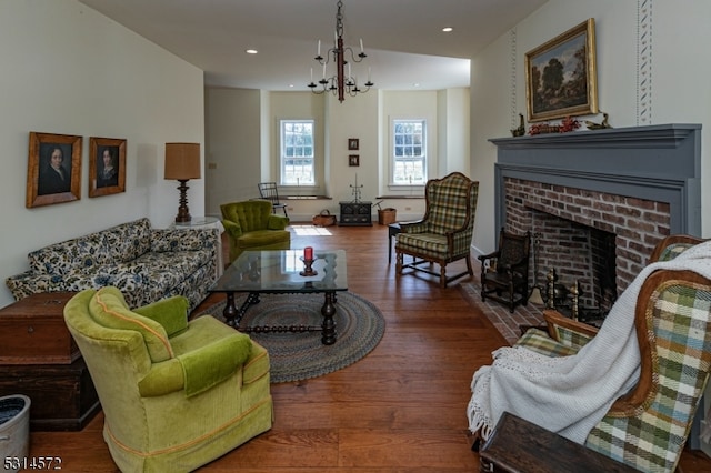 living room with a notable chandelier, dark wood-type flooring, and a brick fireplace