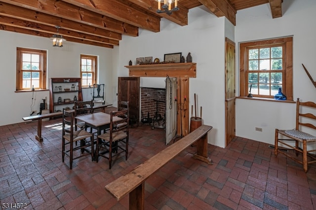 dining space featuring a notable chandelier, beam ceiling, and a brick fireplace