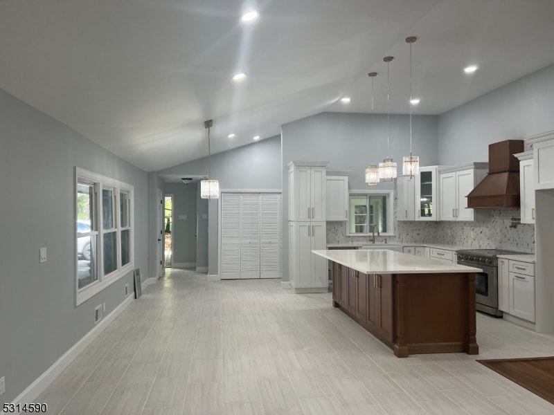 kitchen with custom range hood, vaulted ceiling, a kitchen island, pendant lighting, and stainless steel stove