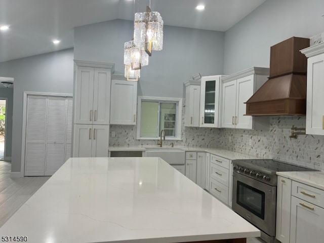 kitchen with sink, stainless steel stove, white cabinetry, decorative backsplash, and decorative light fixtures