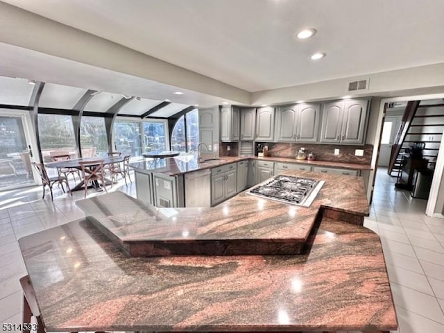 kitchen with appliances with stainless steel finishes, backsplash, light tile patterned floors, gray cabinets, and a kitchen island