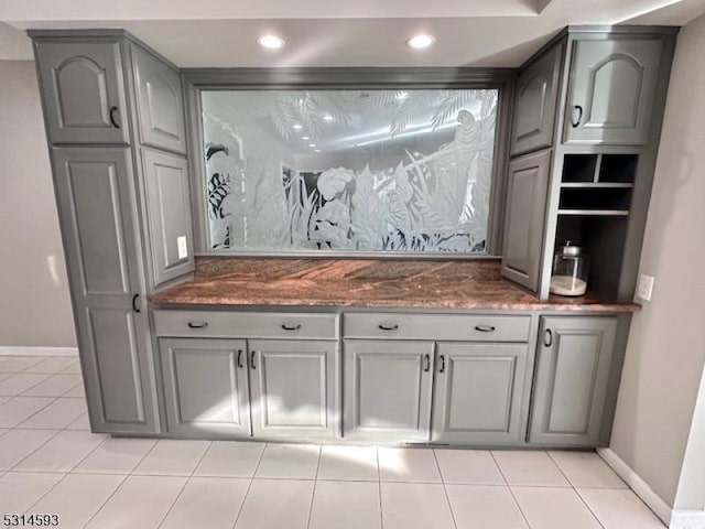 bar featuring gray cabinetry, light tile patterned floors, and dark stone counters