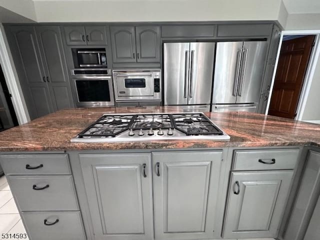 kitchen featuring gray cabinets, dark stone countertops, light tile patterned floors, and stainless steel appliances