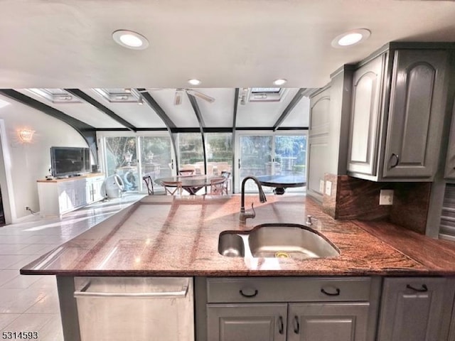 kitchen with gray cabinetry, backsplash, dark stone countertops, and sink