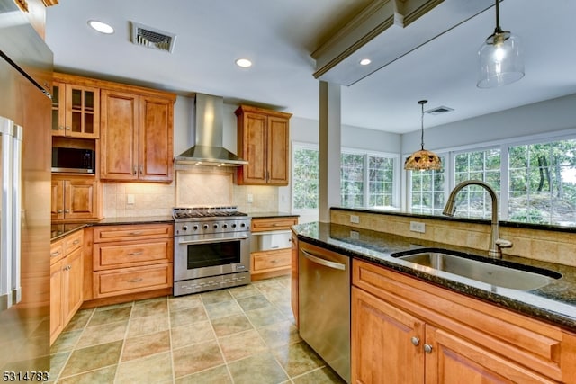 kitchen with wall chimney exhaust hood, appliances with stainless steel finishes, decorative light fixtures, and sink