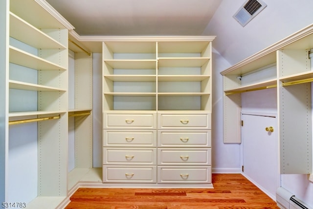 walk in closet with light hardwood / wood-style flooring, vaulted ceiling, and a baseboard heating unit