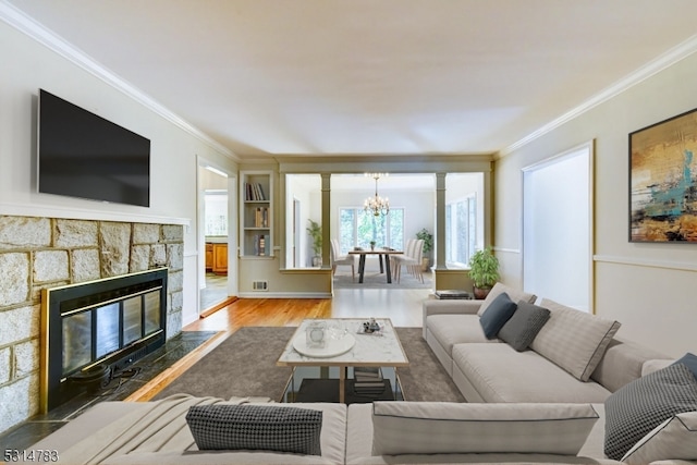 living room with a stone fireplace, a chandelier, hardwood / wood-style floors, and crown molding