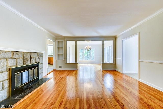 unfurnished living room with ornamental molding, light hardwood / wood-style floors, a notable chandelier, and a stone fireplace