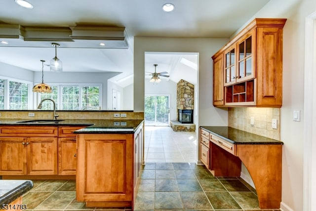 kitchen featuring ceiling fan, sink, a stone fireplace, decorative light fixtures, and vaulted ceiling