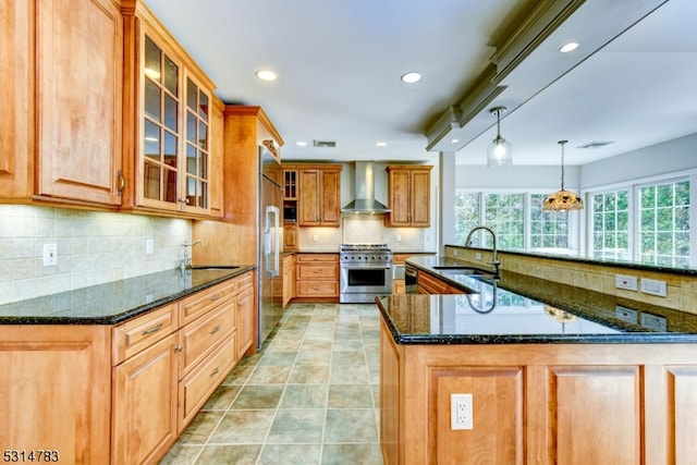 kitchen featuring dark stone countertops, wall chimney exhaust hood, premium appliances, decorative light fixtures, and sink