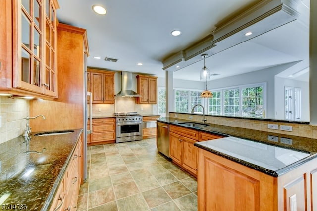 kitchen featuring sink, wall chimney exhaust hood, backsplash, stainless steel appliances, and dark stone counters