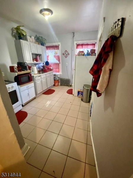 interior space with light tile patterned flooring, white cabinetry, white gas stove, and radiator