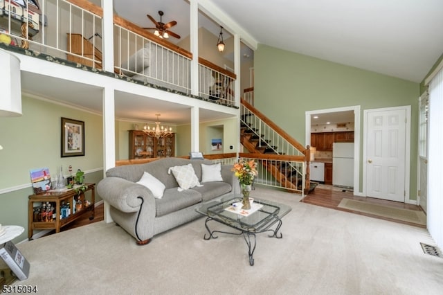 carpeted living room featuring ceiling fan with notable chandelier, ornamental molding, and high vaulted ceiling