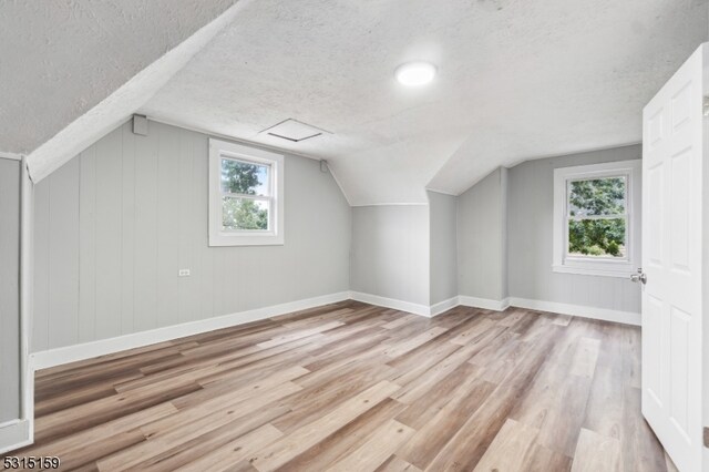 additional living space with a textured ceiling, light wood-type flooring, lofted ceiling, and a healthy amount of sunlight