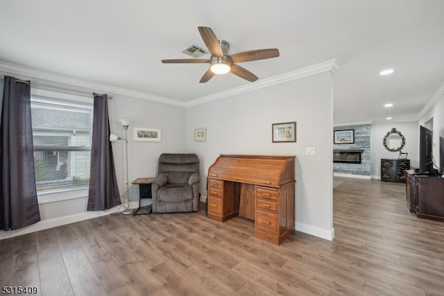 living area featuring ceiling fan, a stone fireplace, light wood-type flooring, and crown molding