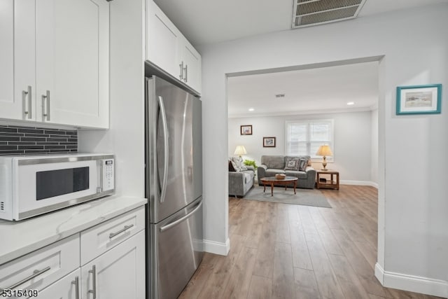 kitchen with stainless steel fridge, white cabinetry, crown molding, light hardwood / wood-style floors, and decorative backsplash