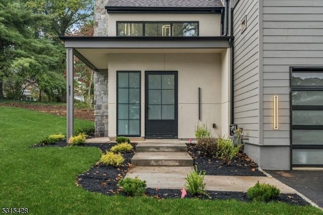view of exterior entry featuring a shingled roof, stucco siding, stone siding, and a lawn