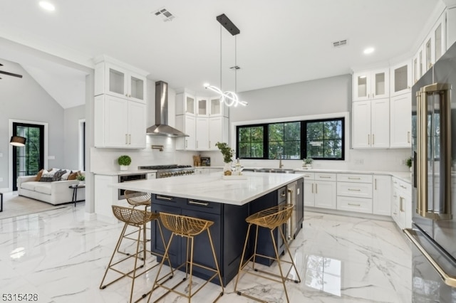 kitchen with a breakfast bar, light stone counters, white cabinets, a kitchen island, and wall chimney exhaust hood