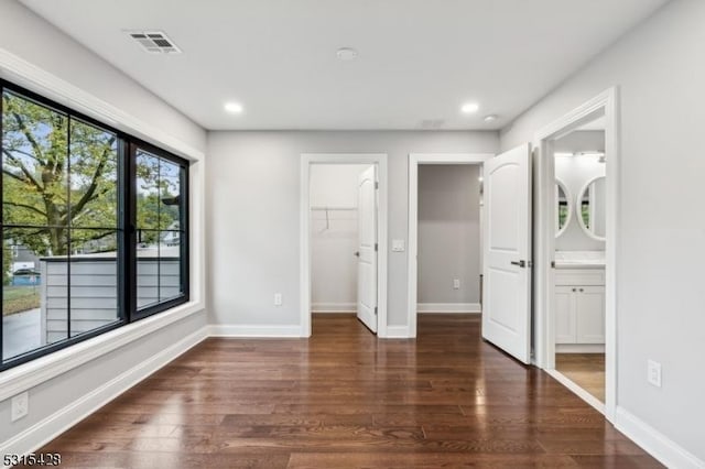 unfurnished bedroom featuring wood finished floors, baseboards, a spacious closet, and visible vents