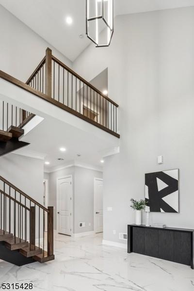 stairway with a towering ceiling, baseboards, recessed lighting, crown molding, and marble finish floor