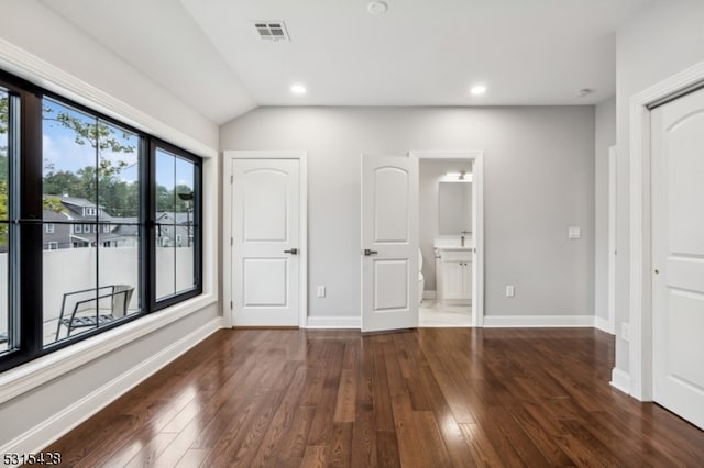 unfurnished bedroom featuring lofted ceiling, ensuite bathroom, and dark wood-type flooring