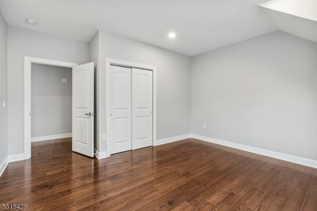 unfurnished bedroom featuring lofted ceiling, a closet, and dark wood-type flooring