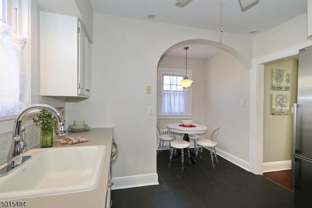 kitchen with pendant lighting, freestanding refrigerator, white cabinets, a sink, and baseboards